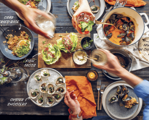 Top-down view of a seafood-based meal spread with hands hands actively cheers-ing